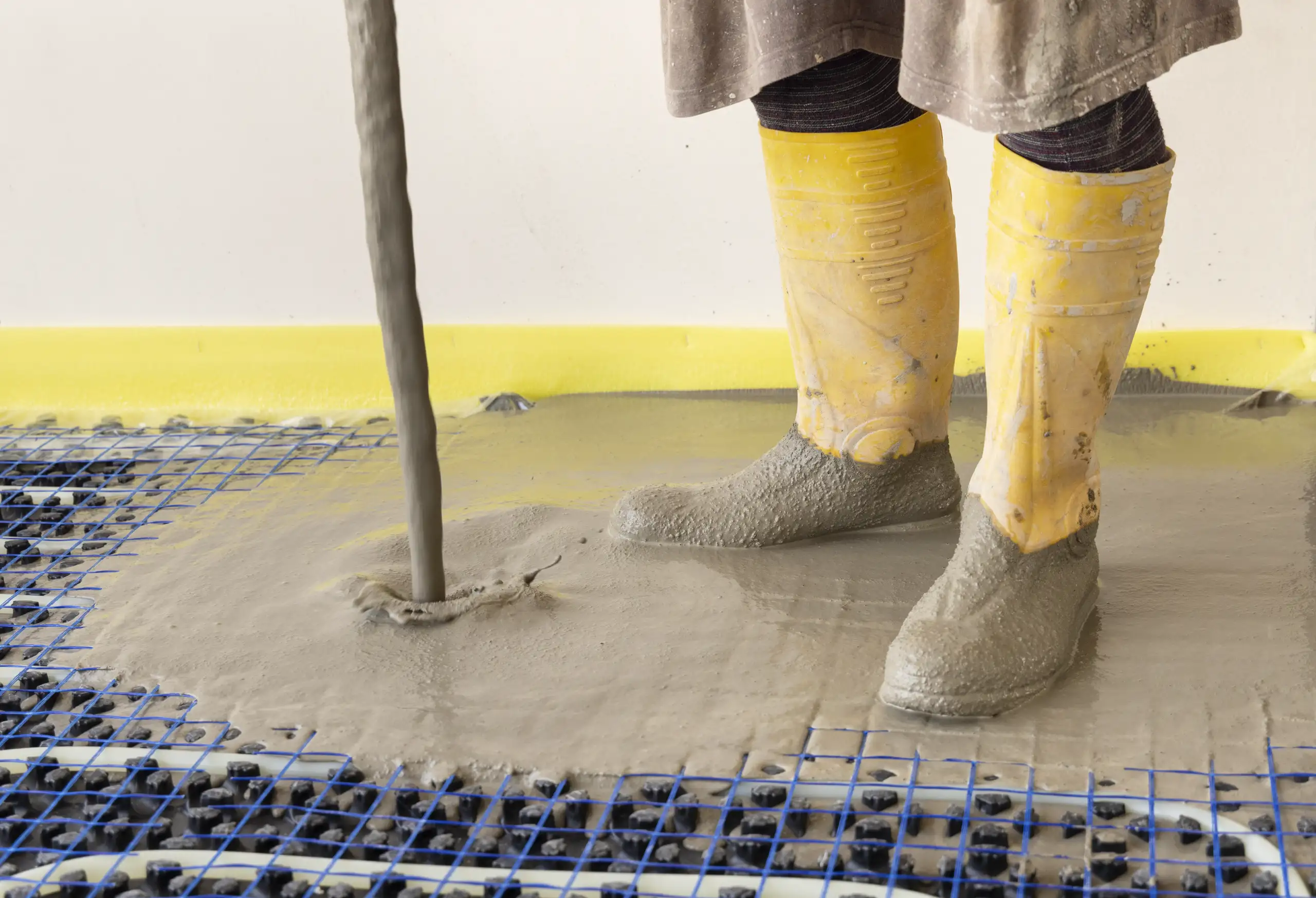 Arbeiter in gelben Gummistiefeln bei der Betonverlegung auf einem vorbereiteten Untergrund
